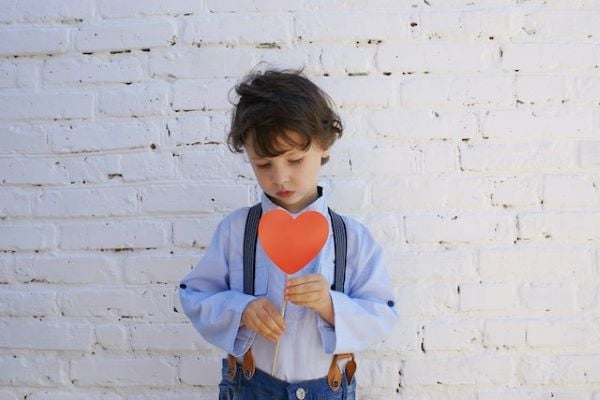 малко момче със синя риза, дънки и тиранти, което държи сърце