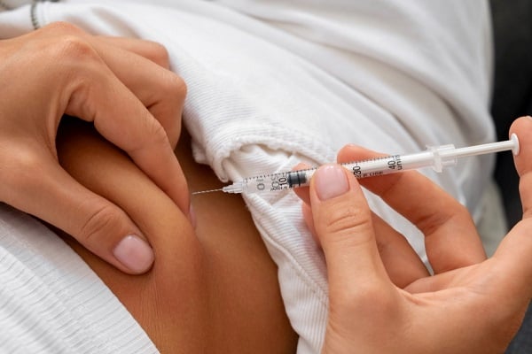Жена с бяла рипсена блуза, която си инжектира инсулин в корема