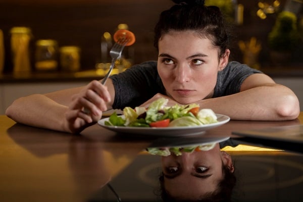 Жена с тъмносива тениска, която гледа вилица, на която е забодено парче домат