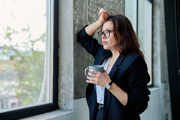Жените в менопауза са два пъти по-застрашени от биполярно разстройство жена с тъмно сако и очила, която гледа през прозорец