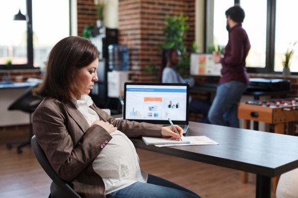бременна жена с тъмна коса, седнала на бюро, държи химикал