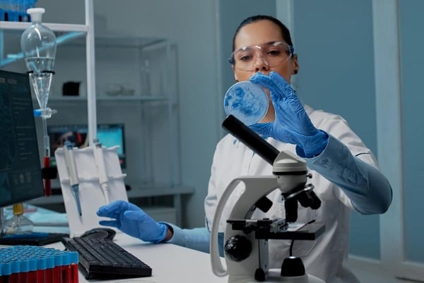 Жена в лаборатория с предпазни очила разглежда съд на Петри
