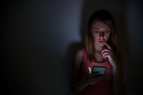 жена в тъмното с телефон в ръка