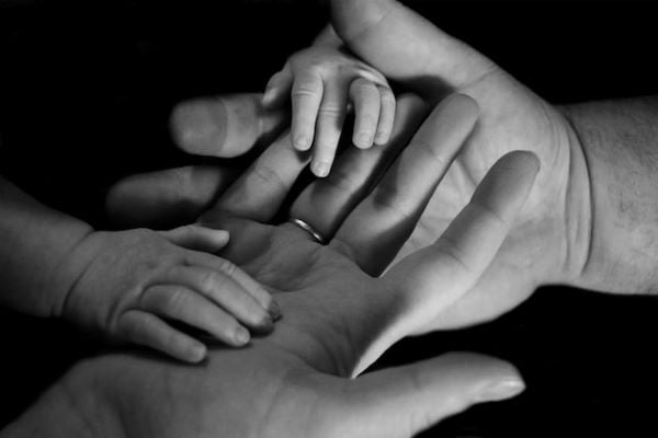 черно-бяла снимка на мъжка и женска длан, държащи бебешка ръчичка