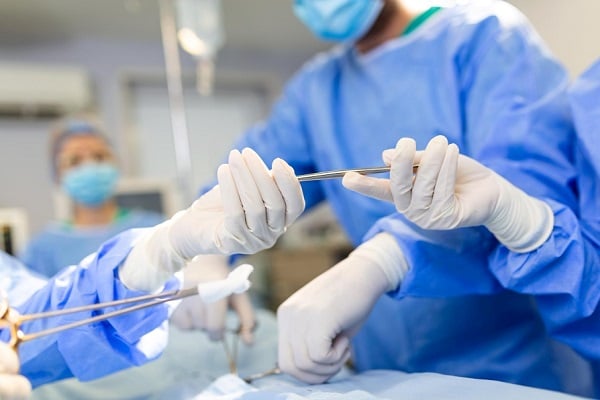 Хирурзи в сини дрехи, които си подават инструмент в операционната