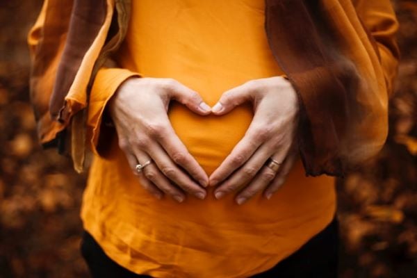 бременна жена с оранжева блуза, длани оформят сърце