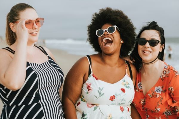 Три млади момичета със слънчеви очила на плаж се смеят