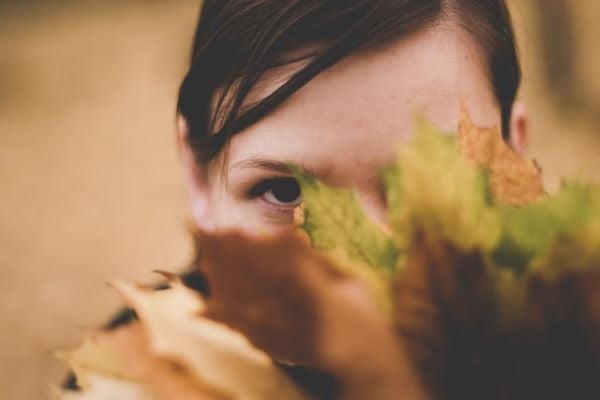 жена крие лице зад есенно листо