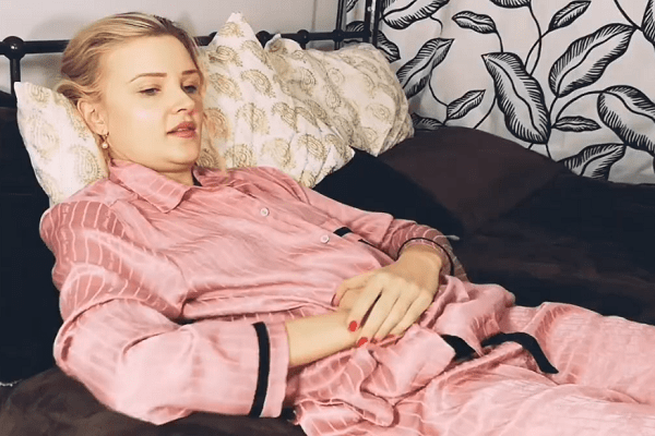 Руса жена с розова сатенена пижама, която масажира с длани коремната област