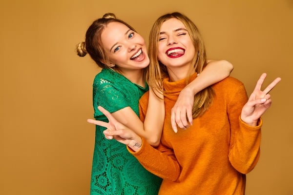 Две тийнейджърки със зелена и оранжева блузи са се прегърнали и се усмихват