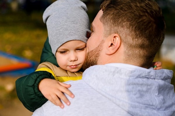 Баща целува малко момченце със сива шапка