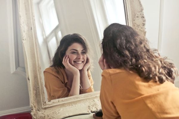 Жена с оранжева риза, която се усмихва в огледалото