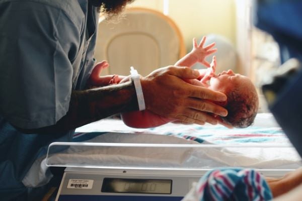 лекар държи новородено бебе над везна