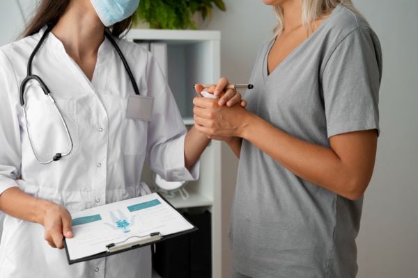 жена лекар с бяла престилка и стетоскоп и пациентка със сива блуза