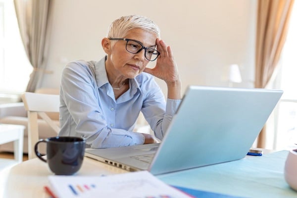 Жена със светлоруса къса коса и очила гледа замислено в екрана на лаптоп