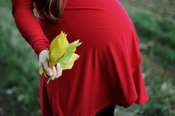 Бременна жена с червена рокля, която държи есенни листа в ръката си