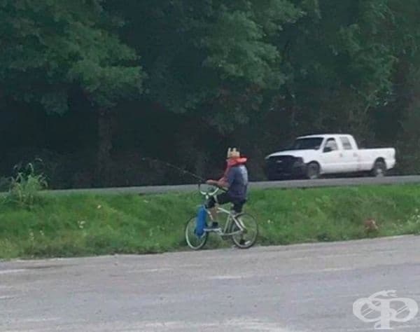 Този мъж лови риба върху колелото си в празно езеро. Той е със спасителна жилетка и корона.